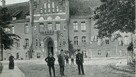 Przedwojenna pocztówka przedstawiająca mężczyzn na tle budynku ówczesnego Starostwa Powiatowego